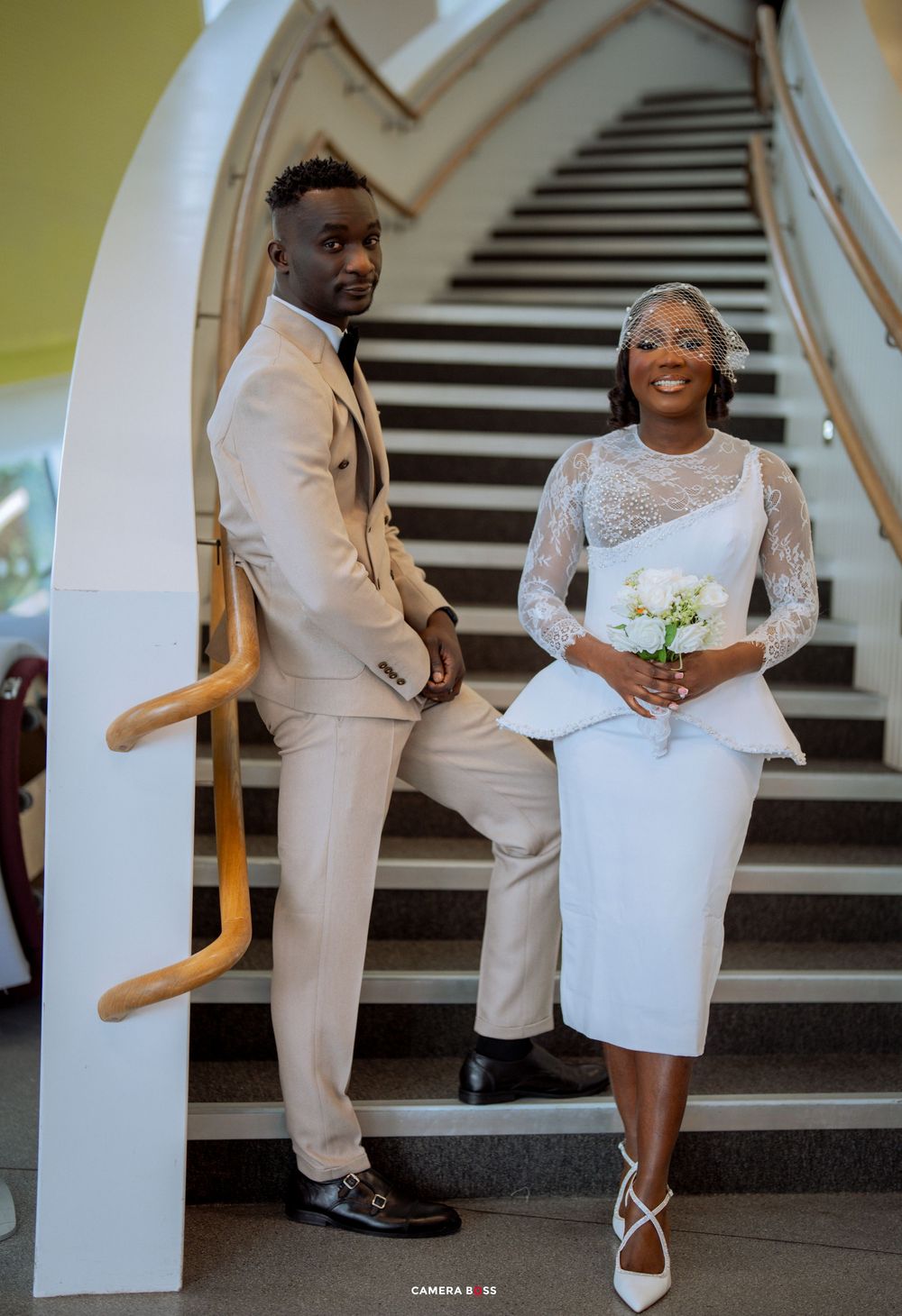 Elegant wedding couple in white outfits pose together on grand staircase for romantic photoshoot series.