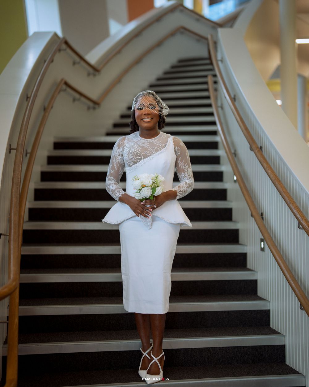 A white short wedding dress is displayed on a grand staircase with black and white striped steps.