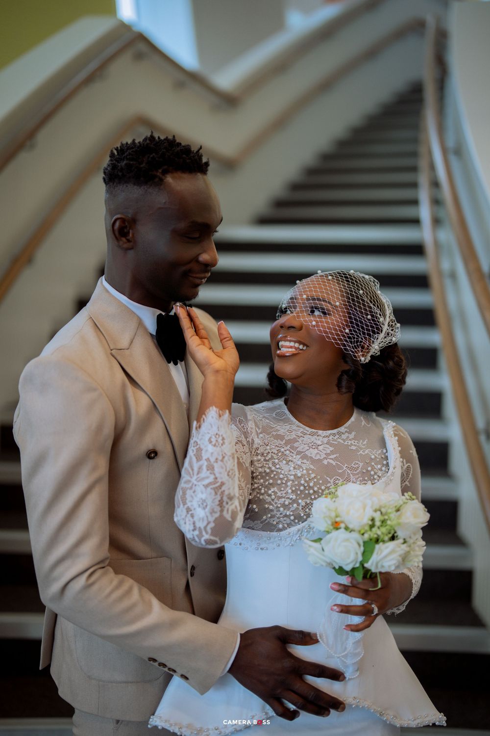 A joyful wedding couple shares intimate moments and laughter while posing on a staircase in formal attire.