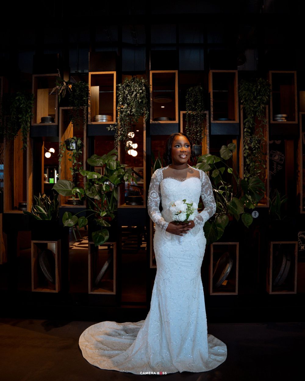 A series of elegant wedding photos displayed in wooden frames on a dark wall with ambient lighting and greenery.