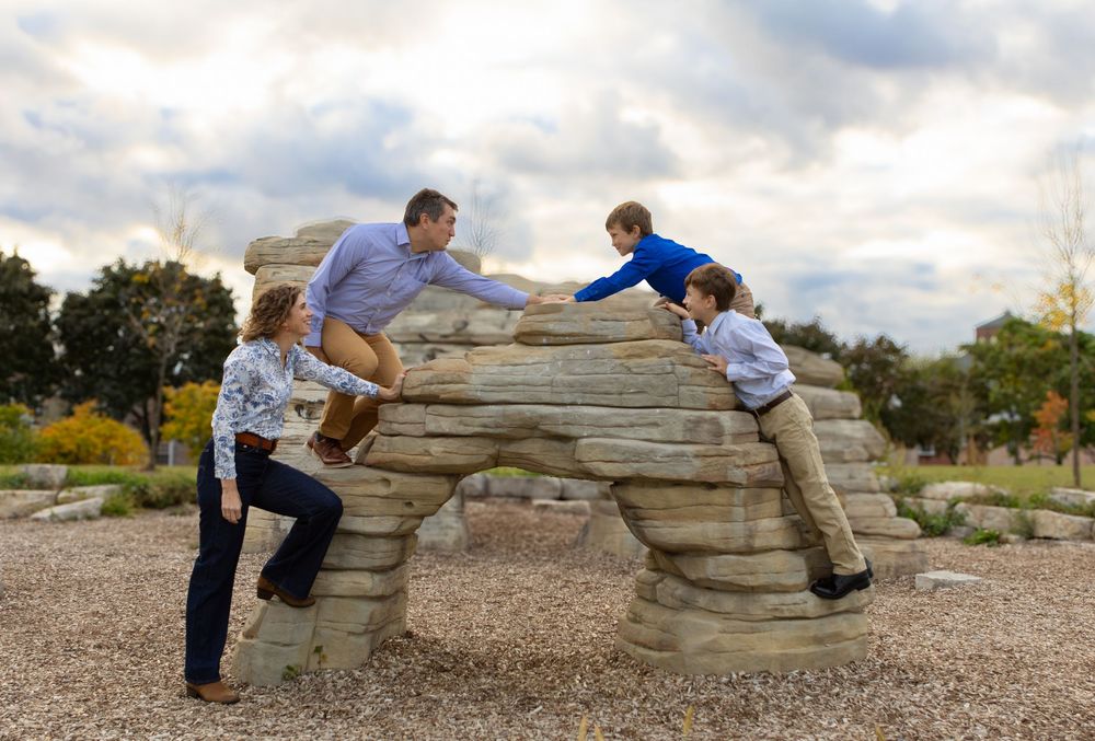 Children playing on natural stone formations in an urban park setting.