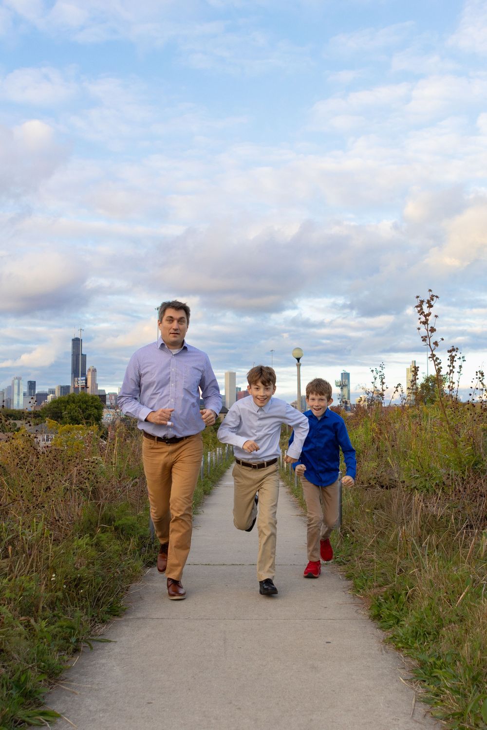 Group walking along a winding path with wildflowers and city skyline in background.
