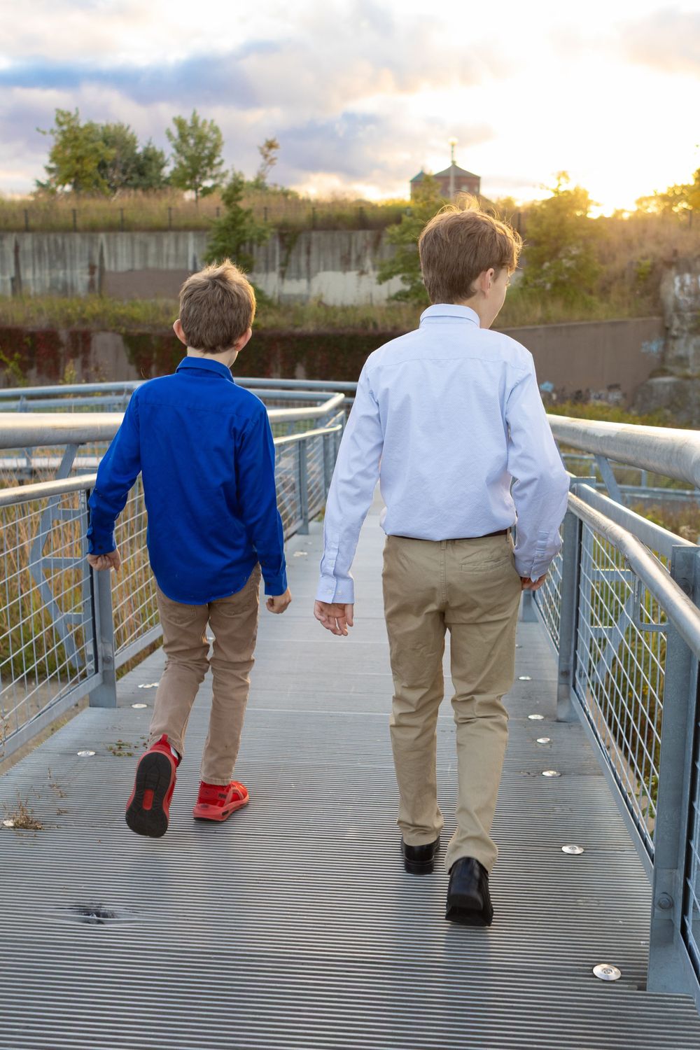 People walking along metal bridge walkway during sunset.