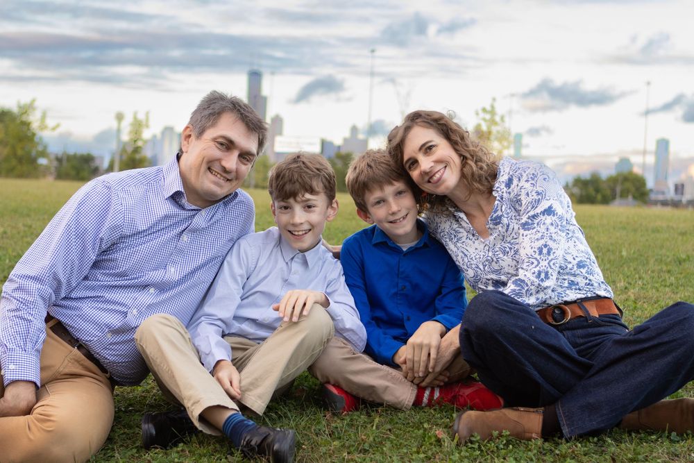 Family relaxing together on grassy hill with urban skyline in background.