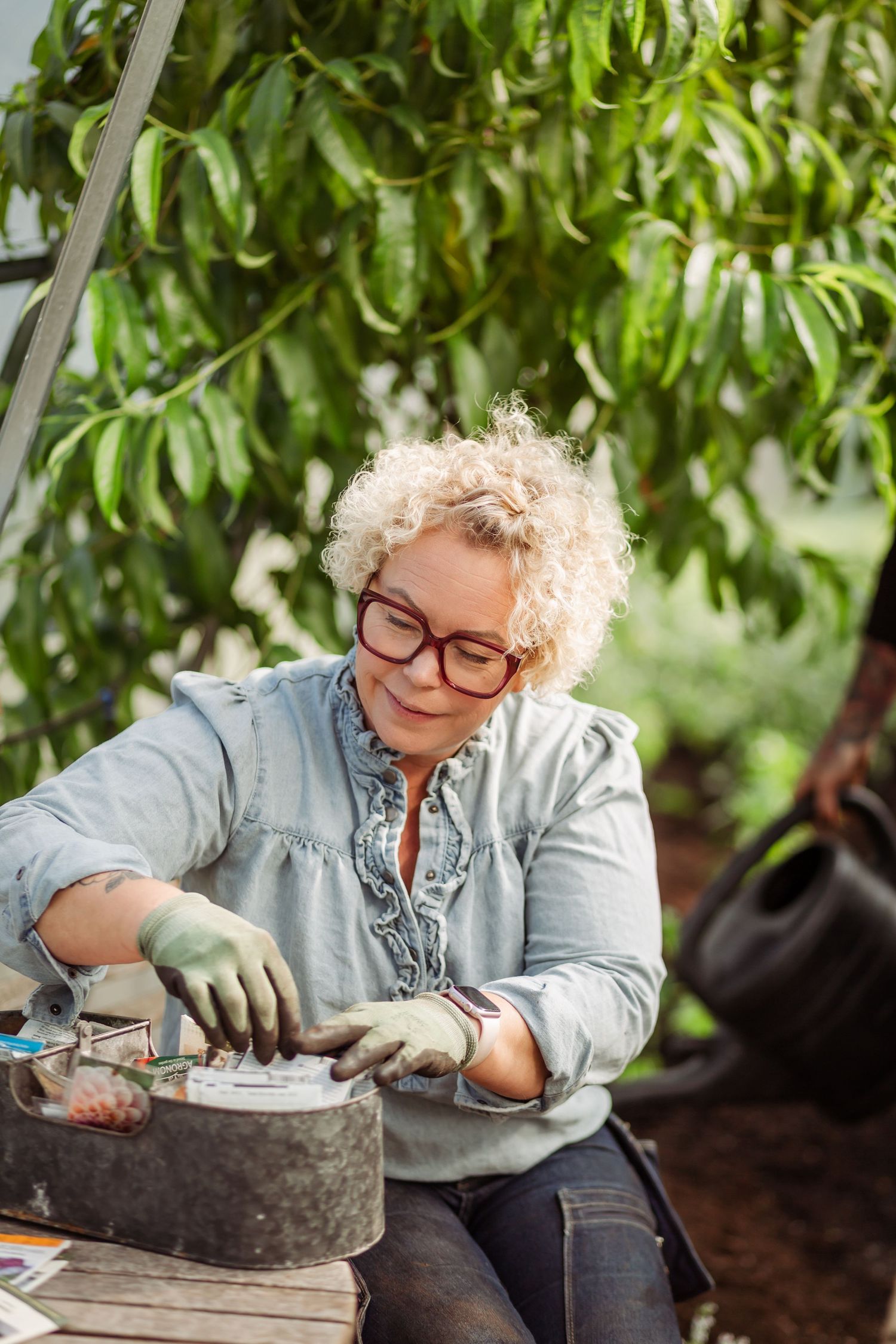 A gardener in denim and gloves works carefully with small plants in a concrete planter outdoors.