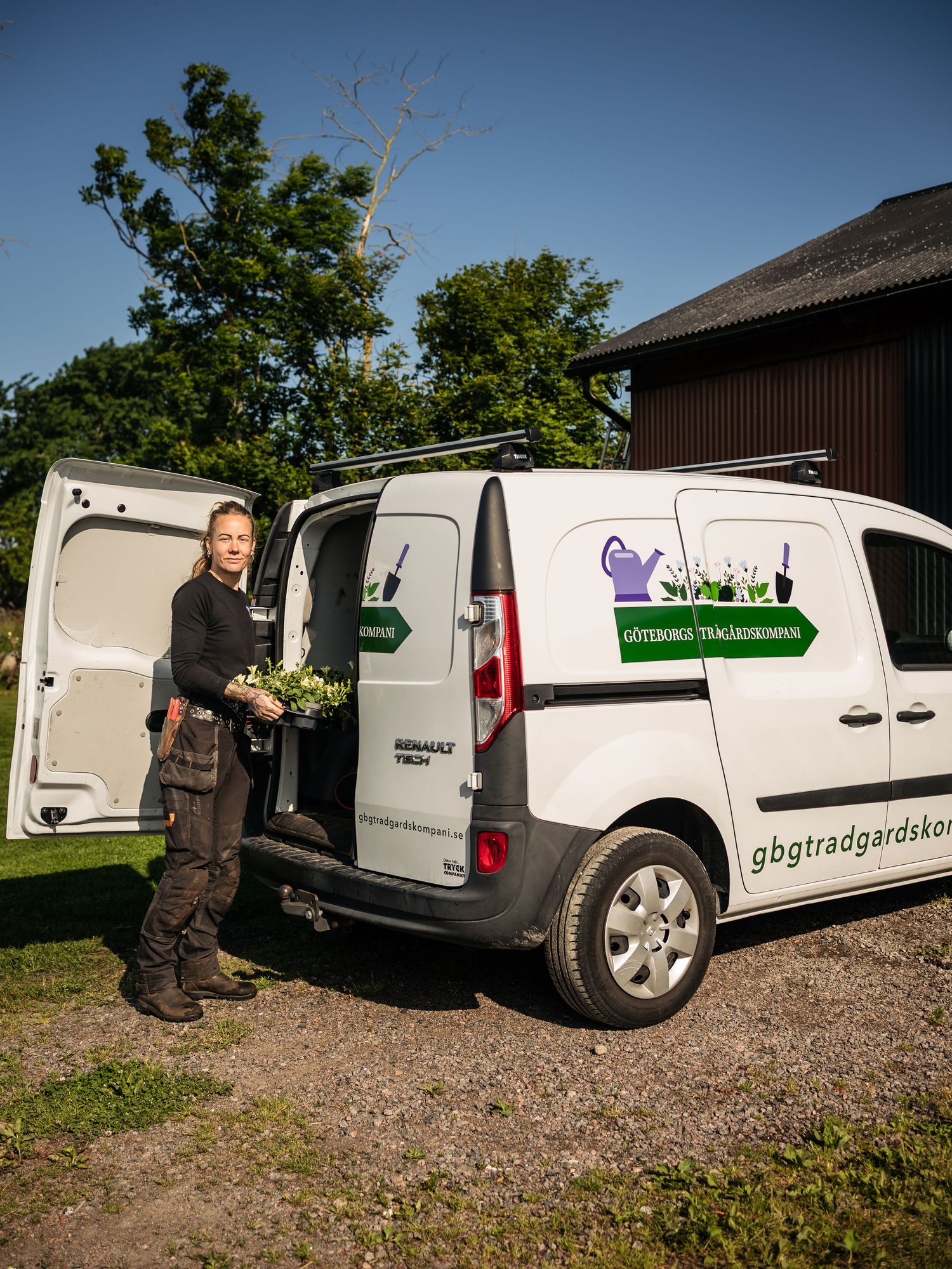 A commercial gardening van with company logo parked outside a wooden building on a sunny day.