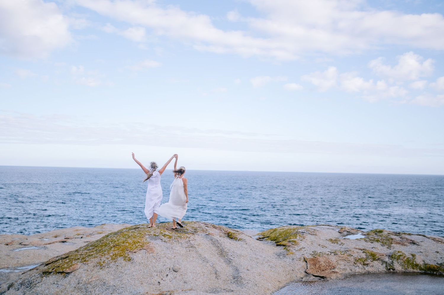 People enjoying a scenic coastal view from a rocky outcrop overlooking the ocean on a sunny summer day.