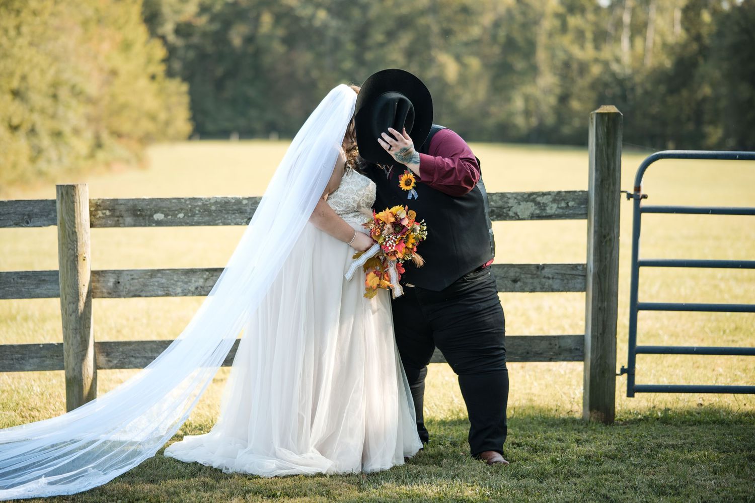 Newlyweds share intimate moments by rustic wooden fence during countryside photoshoot.