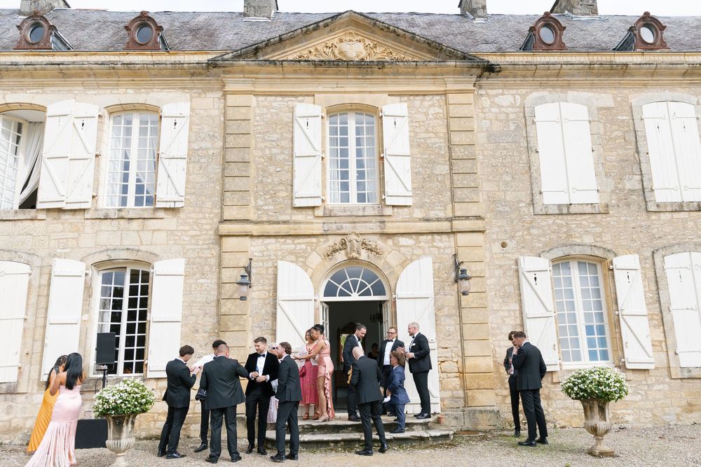 People gather outside a grand historic French chateau with elegant stone architecture and tall windows.