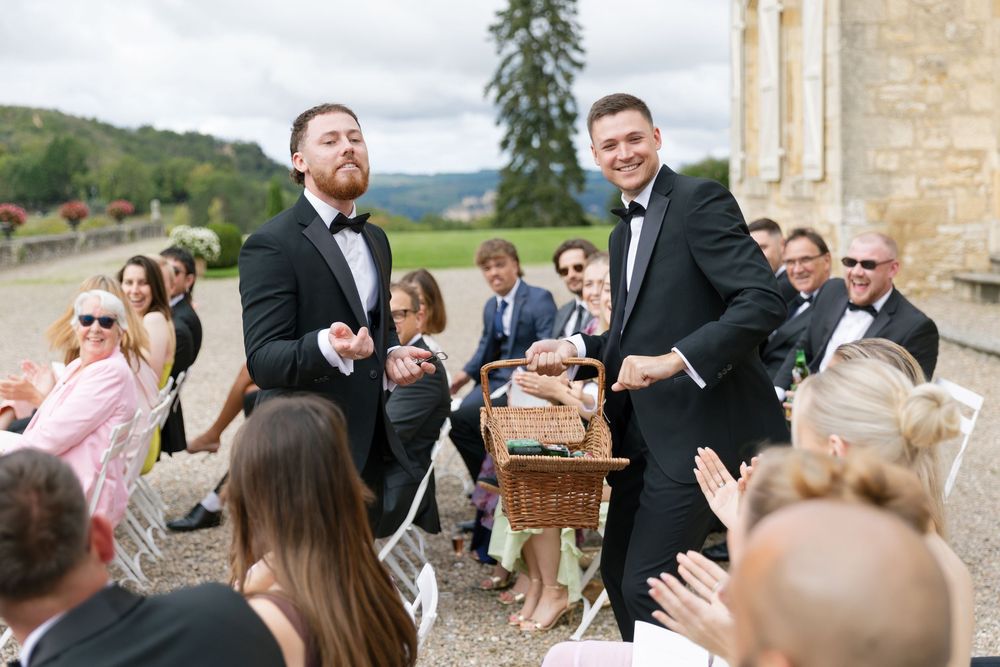 Wedding guests gather outside a historic stone building for a celebratory reception on a sunny afternoon.