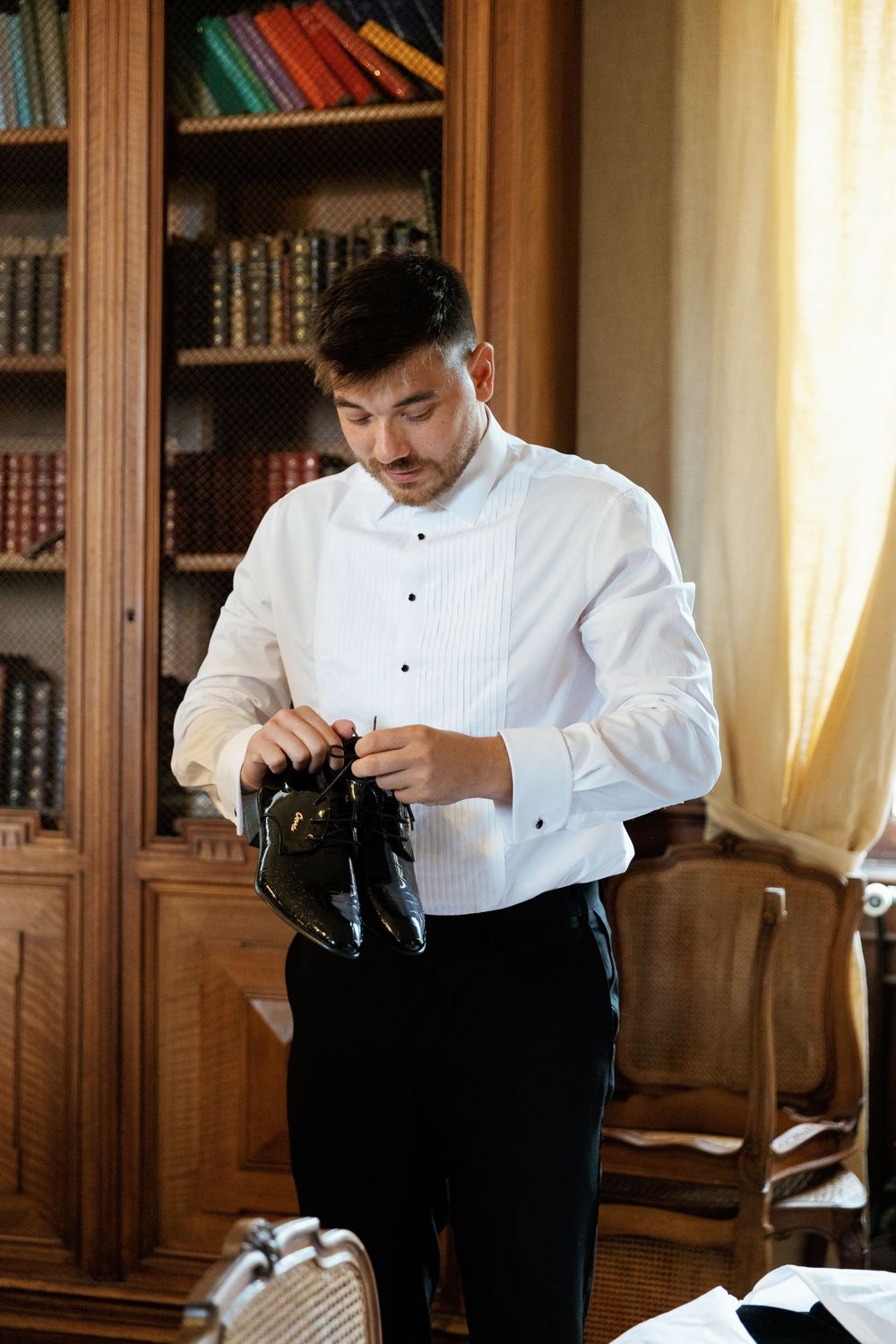 Man in formal attire adjusting his clothing in a wood-paneled library setting.