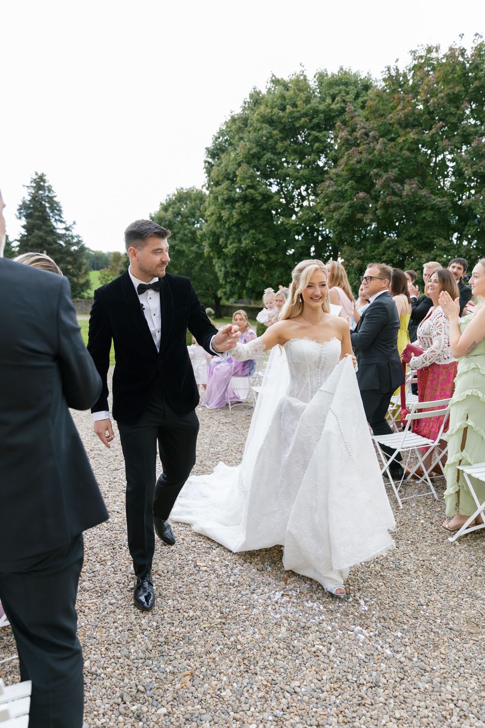 Wedding party and guests mingling on gravel path during outdoor celebration.