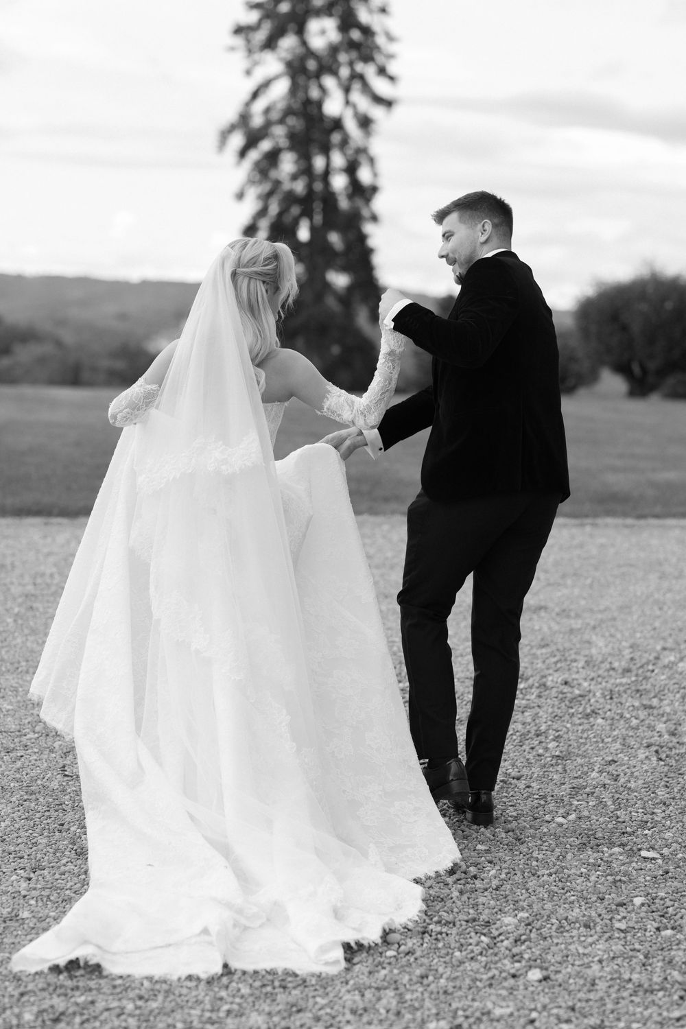 Romantic black and white photo of newlyweds walking together on gravel path.