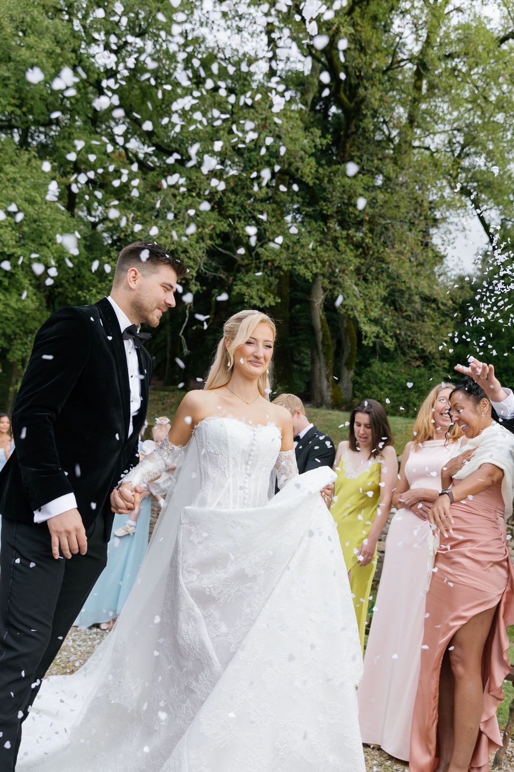 Wedding celebration with confetti being thrown as couple celebrates among guests in pastel attire.