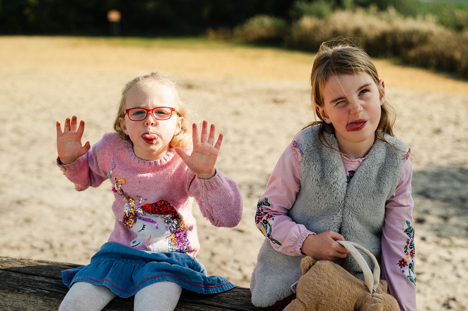 Two children sitting outdoors making silly faces and expressions while playing together in natural light.