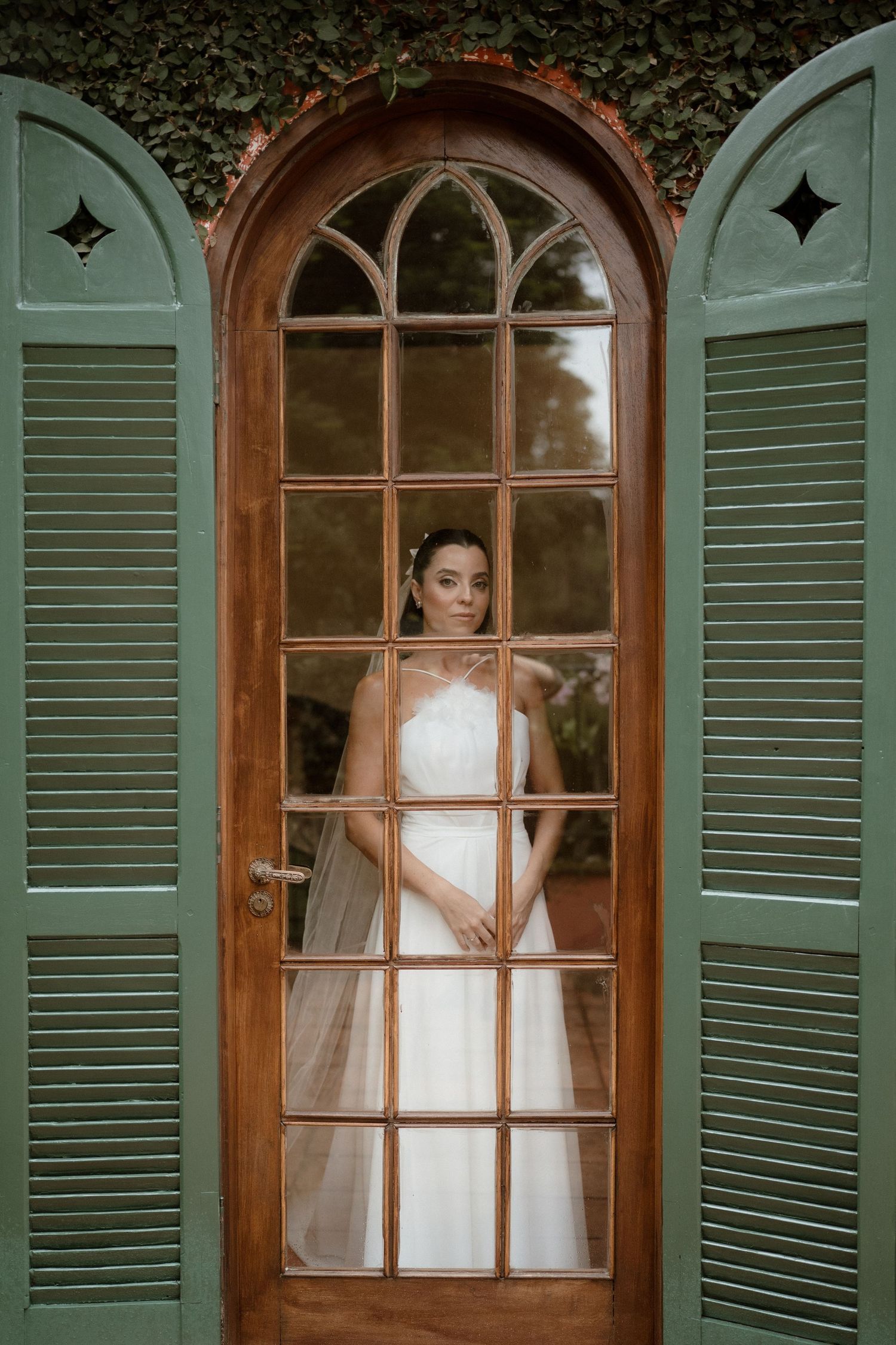 Elegant green shuttered windows with arched tops frame a romantic bridal portrait in soft lighting.