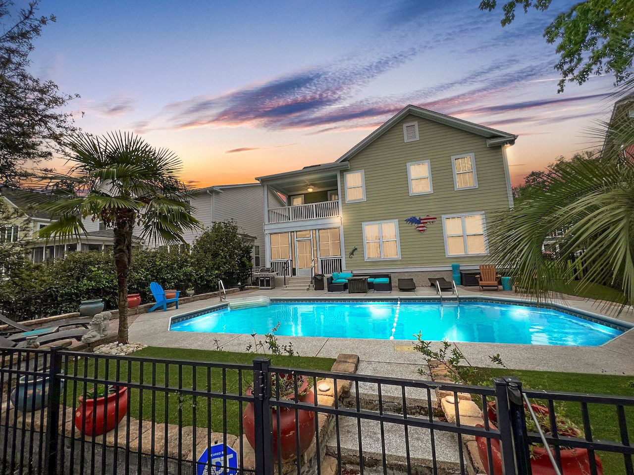 Modern apartment complex with illuminated pool at sunset surrounded by palm trees and outdoor furniture.