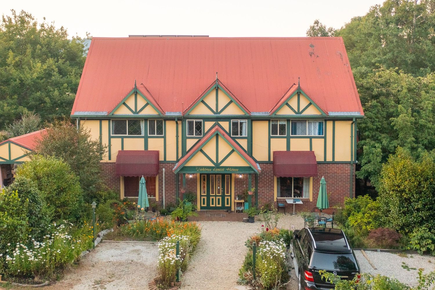 Striking Tudor-style two-storey home with red roof, yellow render and established garden surrounds.