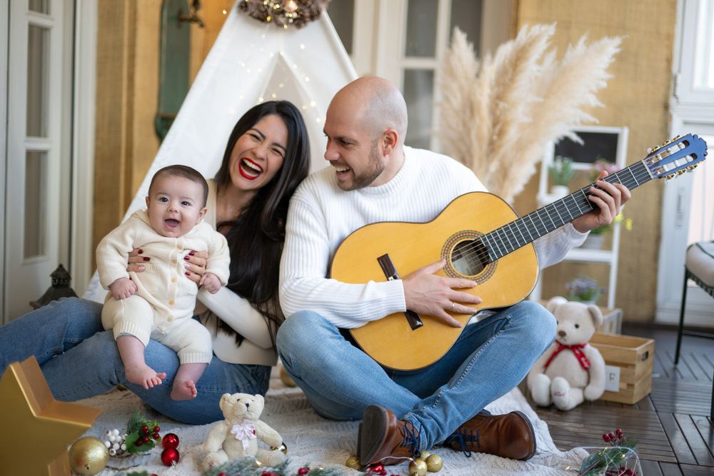 Family sitting on floor playing acoustic guitar and singing together in living room with natural light.