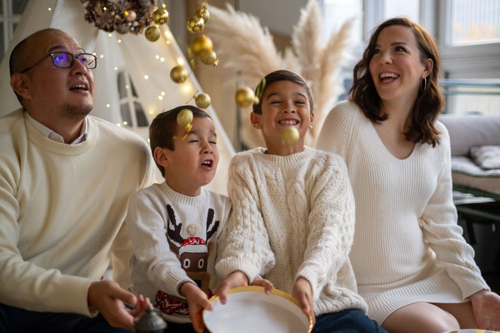 A joyful family wearing cozy white sweaters laughs together while sitting indoors during the holiday season.