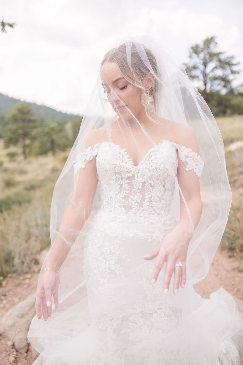 Close-up details of a delicate lace wedding dress with flowing tulle veil against a mountain backdrop.