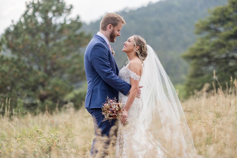 A couple embraces during their wedding photoshoot in a rustic mountain landscape with tall grass.