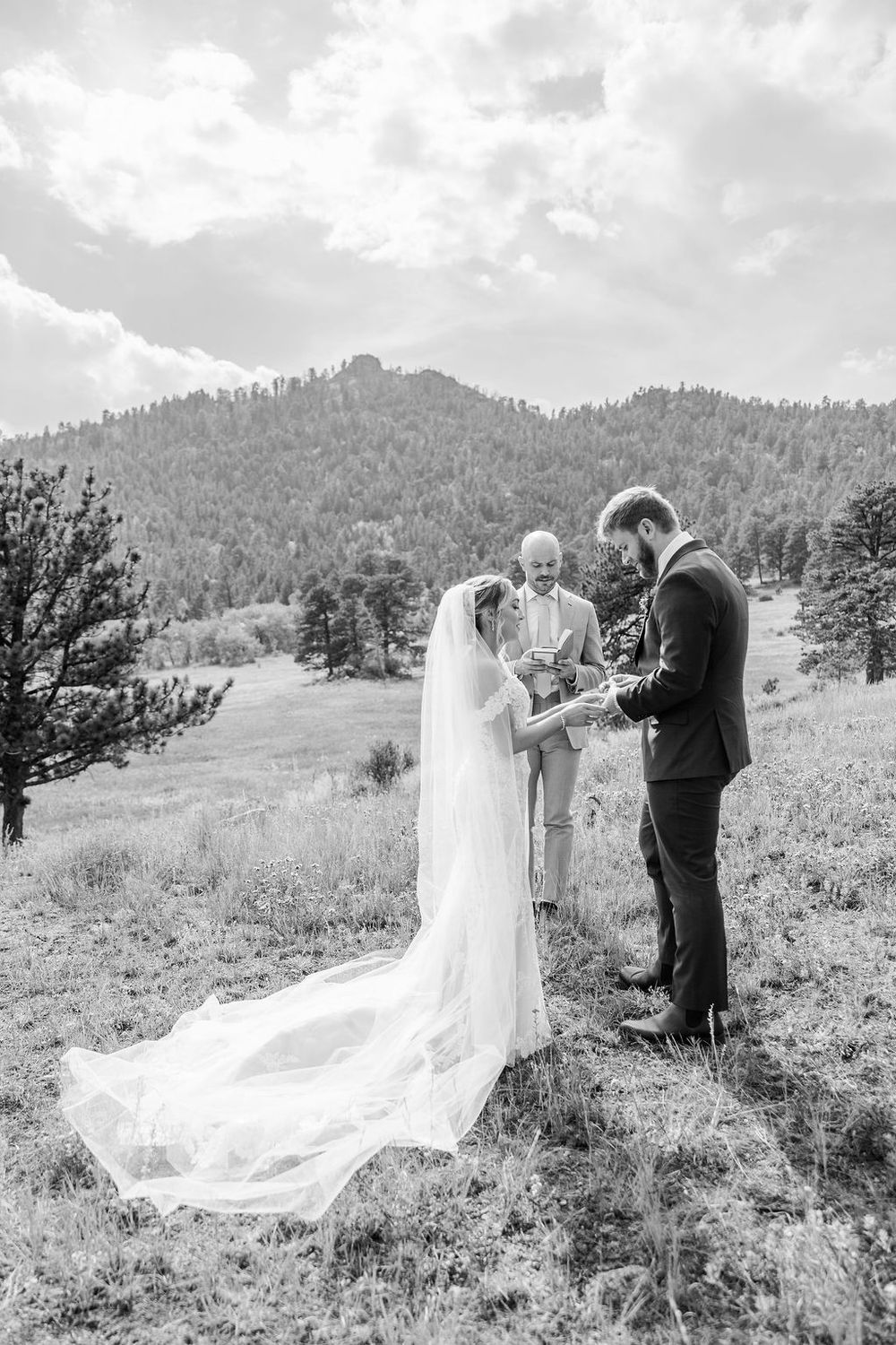 A wedding ceremony takes place on a scenic mountain hillside with flowing white dress and veil catching the breeze.