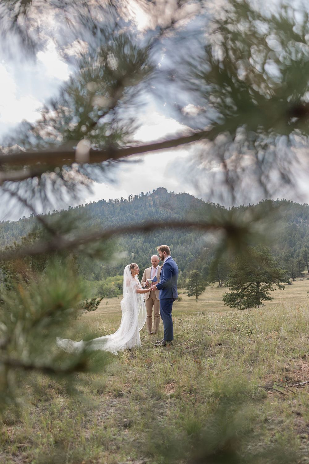 A couple shares an intimate moment during their wedding ceremony against a mountainous Colorado landscape.