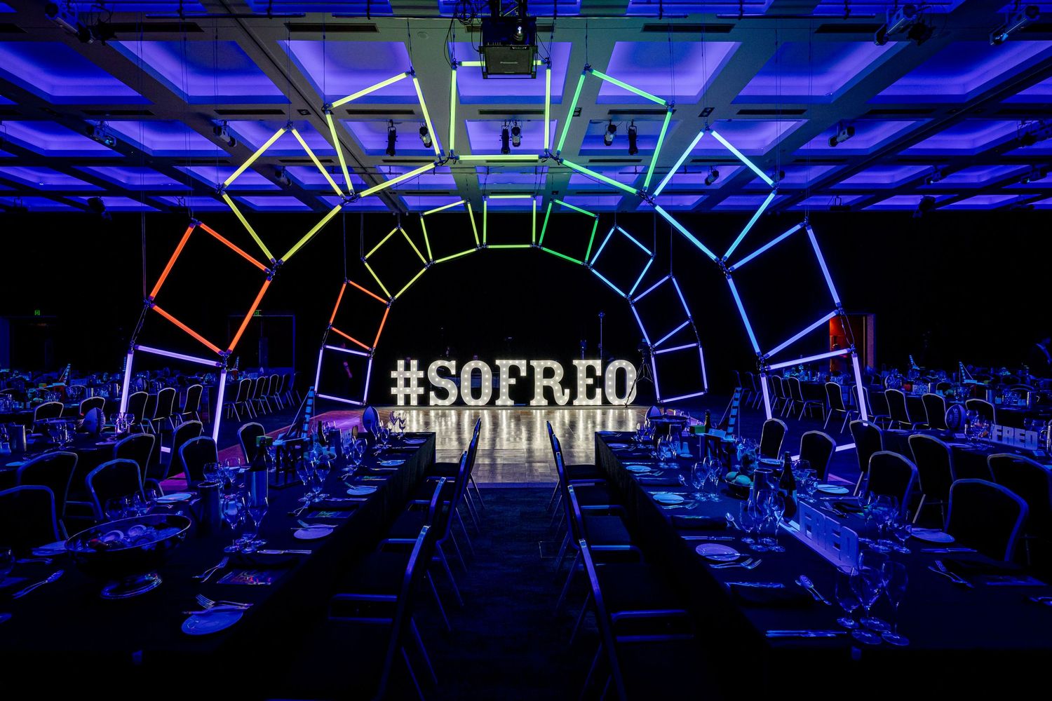 Elegant event venue with purple uplighting and black chairs arranged in rows for a formal gathering.