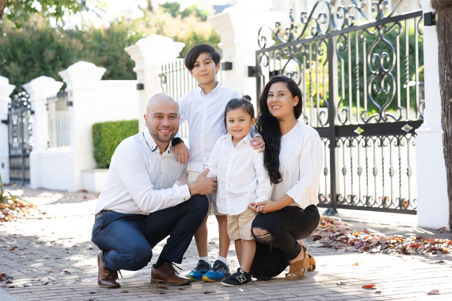 Outdoor family photo session near ornate white gate and garden setting.