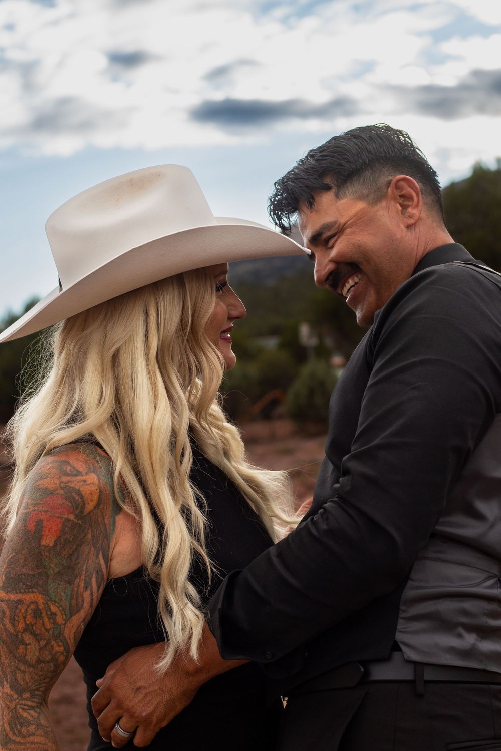A couple shares an intimate moment outdoors, with one wearing a beige hat and the other in dark clothing.