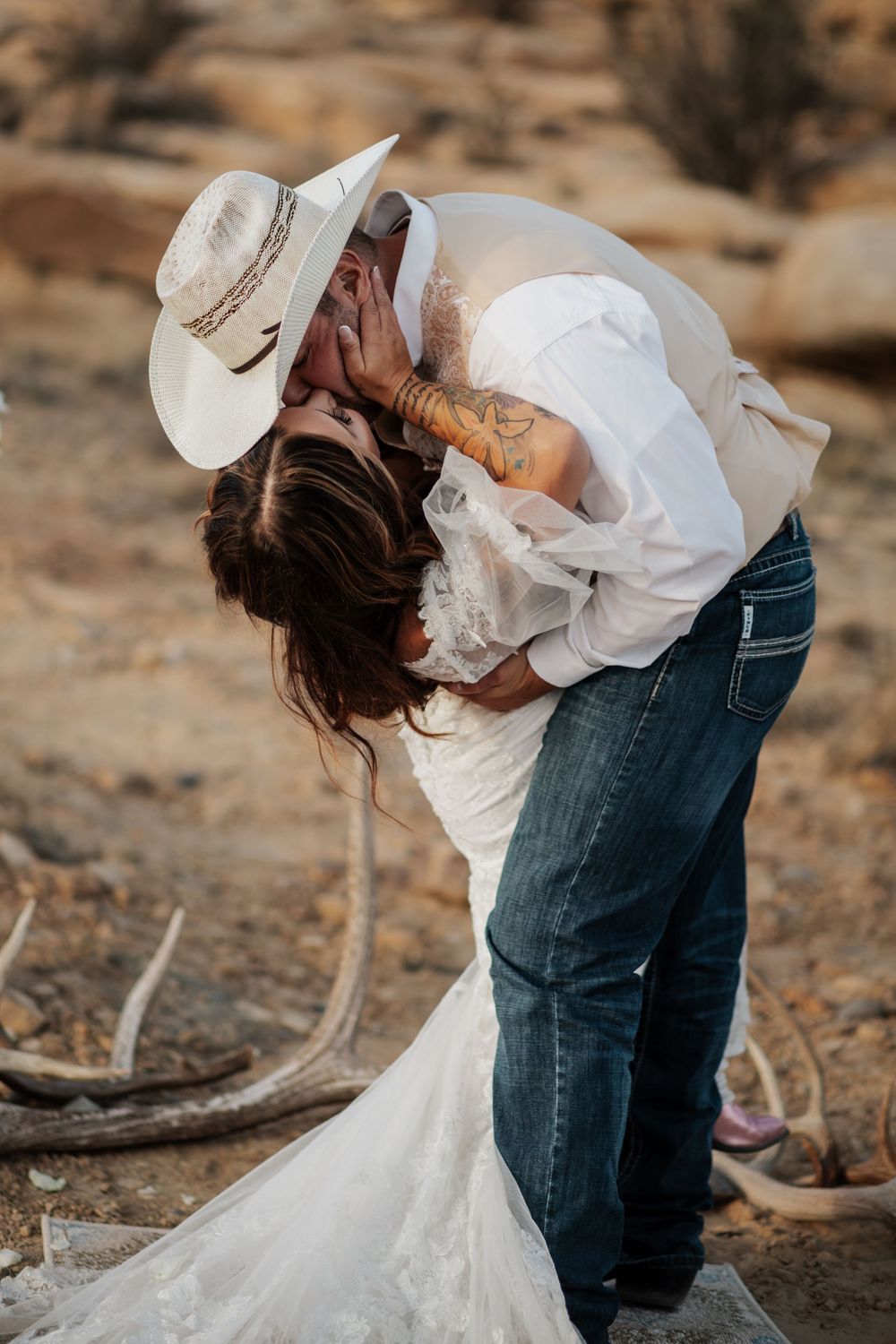 A romantic dip kiss between a couple in western attire during their rustic outdoor wedding photoshoot.