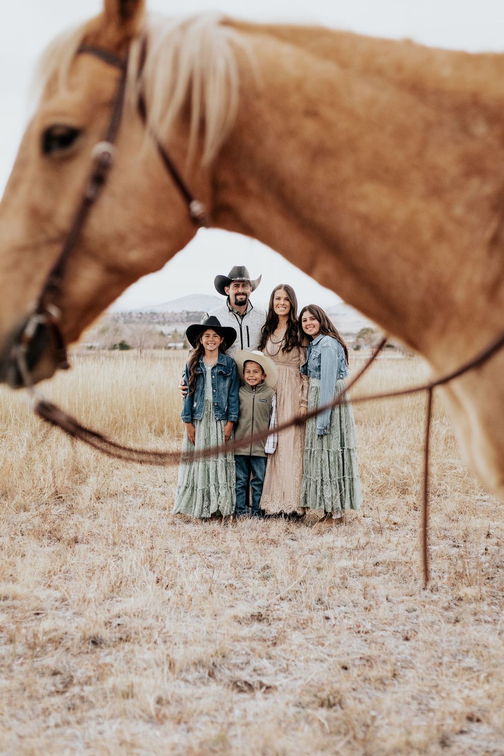 A group poses with brown horses in a rustic field wearing denim and floral dresses for a countryside photoshoot.