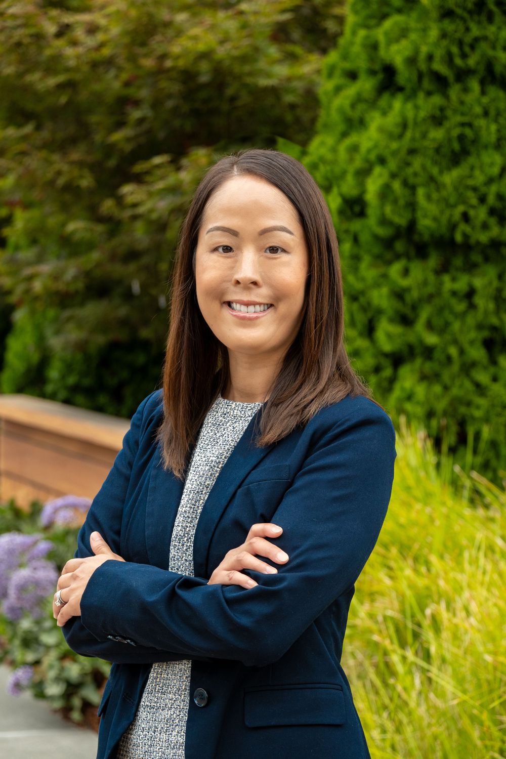 Professional portrait in a navy blazer and patterned top against a vibrant green outdoor background.