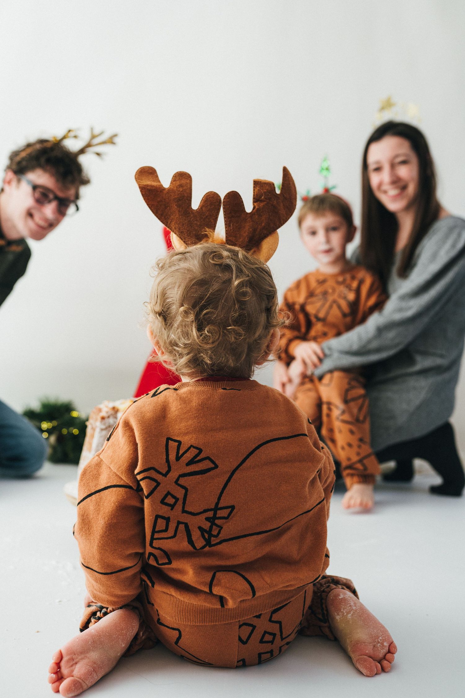 Un enfant de dos portant des bois de renne regarde ses parents pendant une mini-séance de Noël en famille au studio Mon Amour des Photos