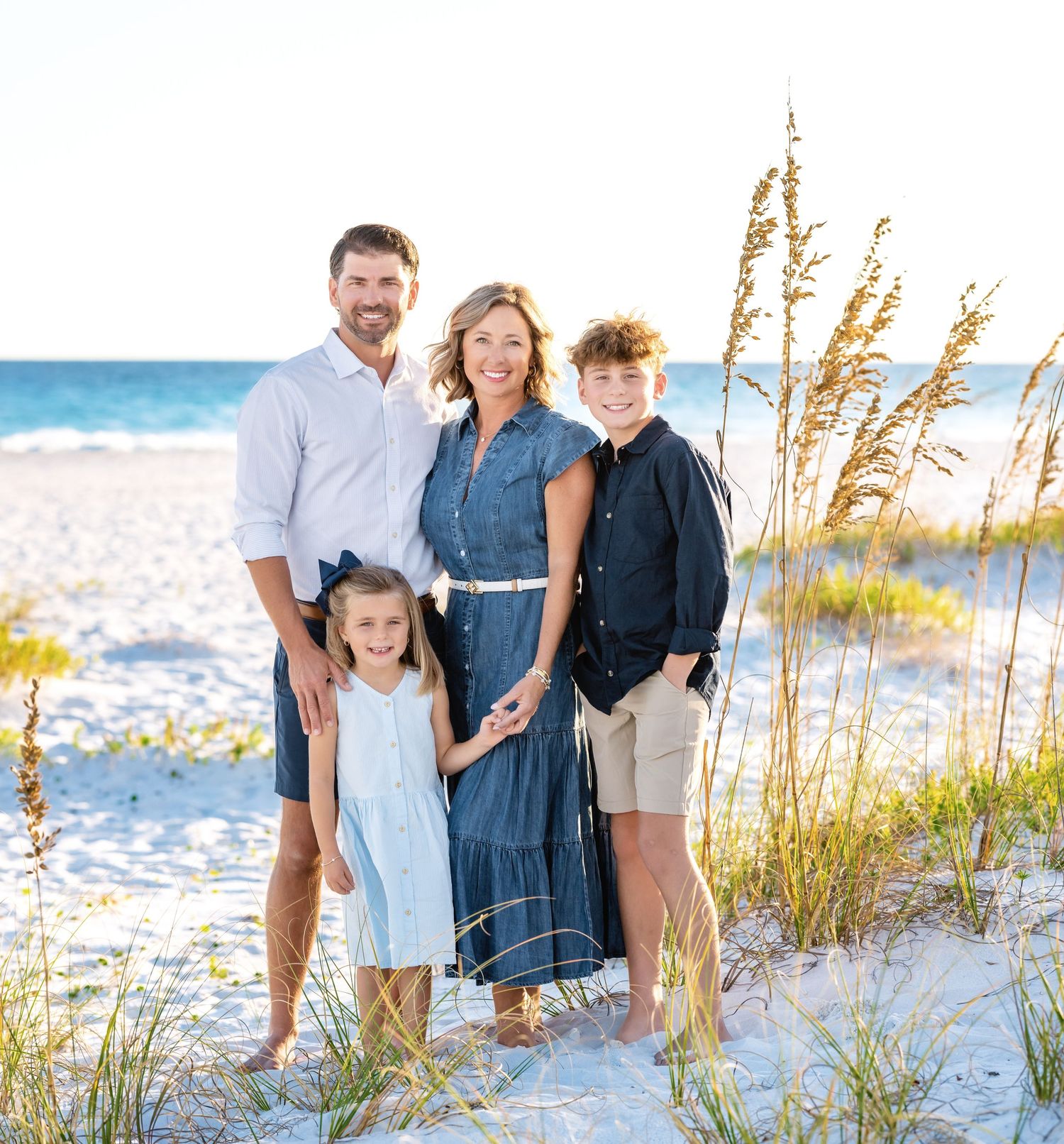 Family enjoying a sunset walk through sea oats and sand dunes on a white sandy beach.