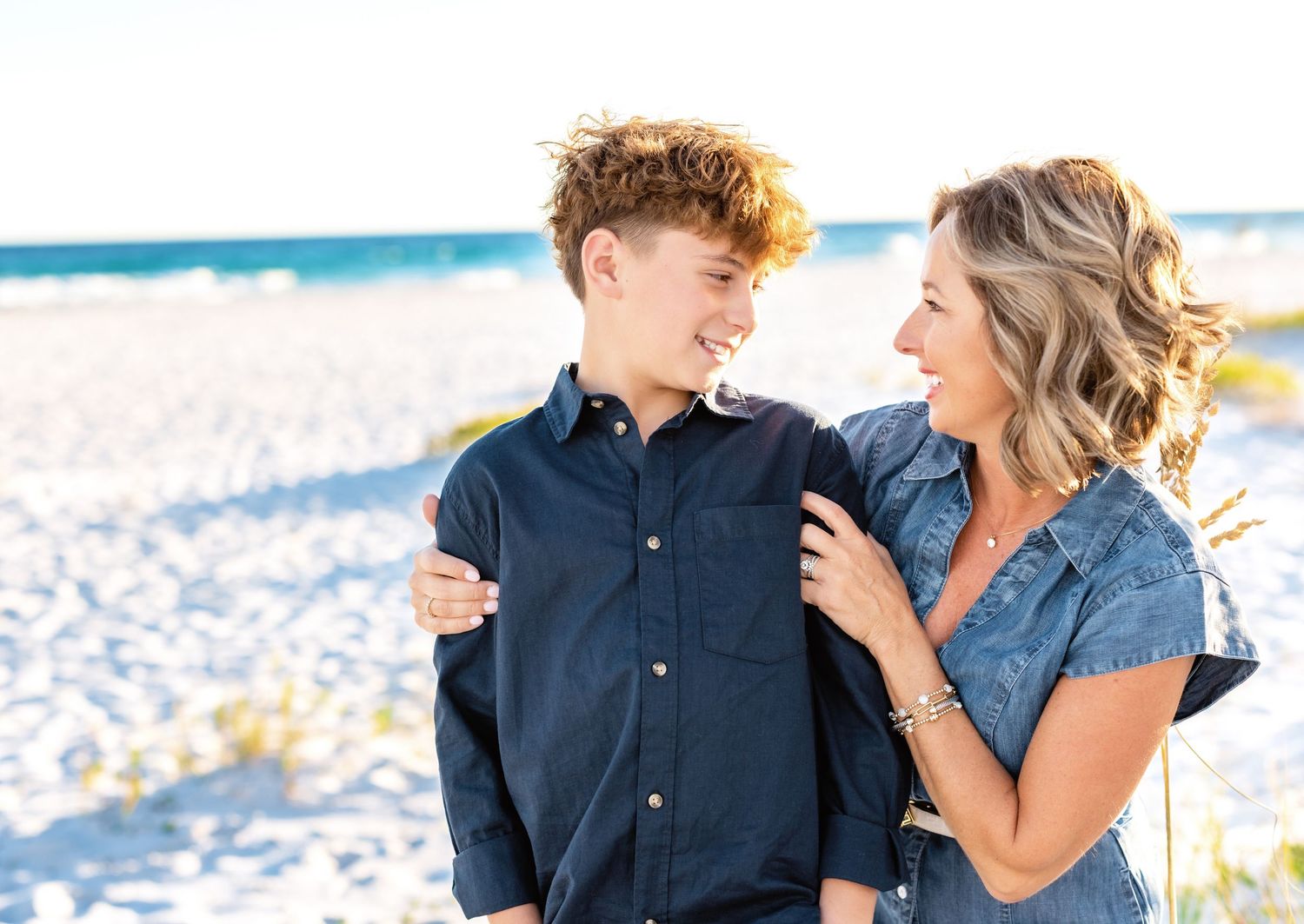Couple sharing intimate moments on a sunny beach during sunset photoshoot.