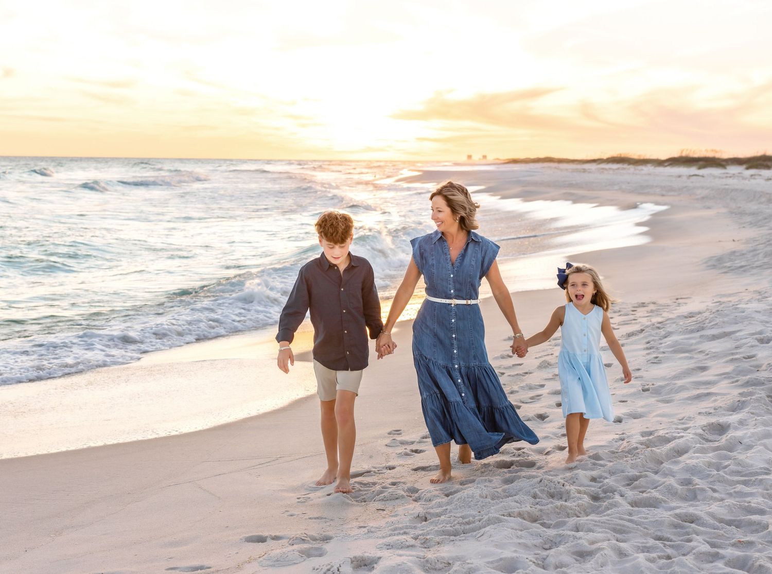 Family walking together along a peaceful beach at sunset with gentle waves rolling in.