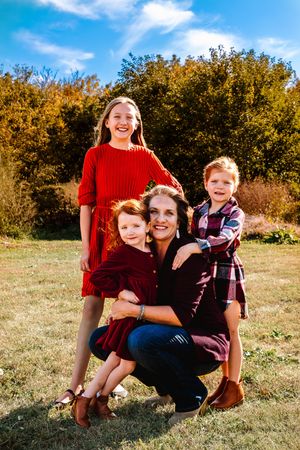 A family enjoys a sunny autumn day together in a grassy field with golden foliage in the background.
