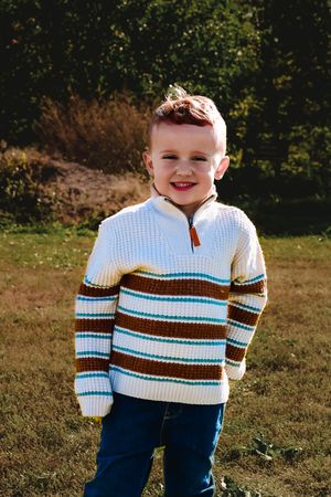 A young child wearing a striped sweater and jeans plays outdoors on a sunny autumn day.