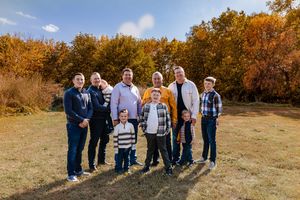 A group of people stand together in a golden autumn field during sunset, casting long shadows on the grass.