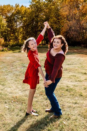 Two people in red and blue outfits dance playfully together in a sunlit autumn field.