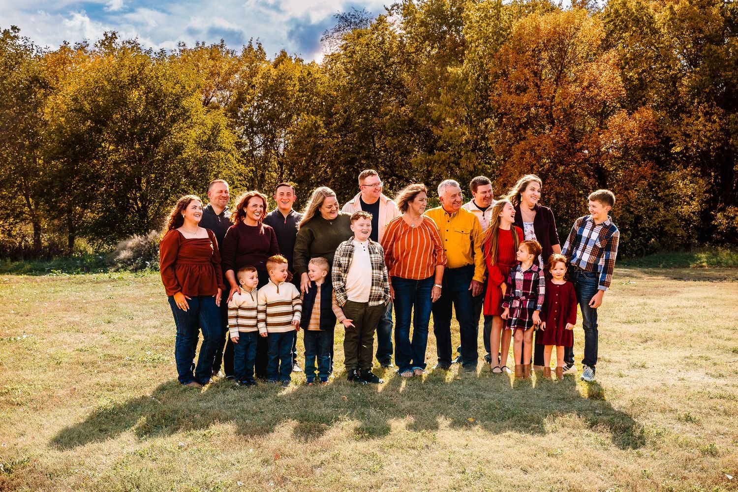 A group of people stands together outdoors against a backdrop of golden autumn trees and blue sky.