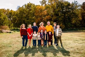 A group of people stand in a line with their backs to the camera against a backdrop of autumn trees and grass.