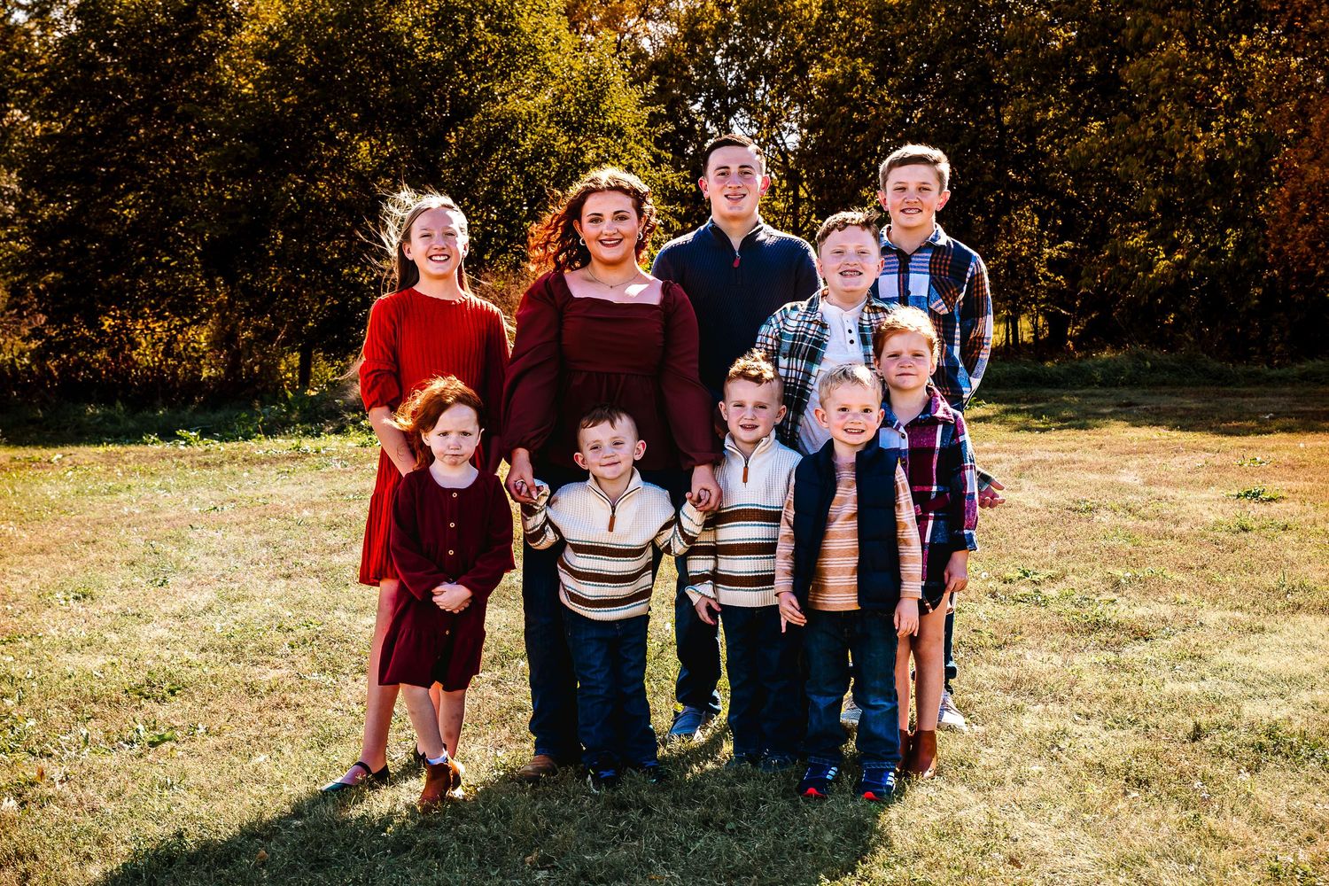 A group in coordinated burgundy, navy and striped outfits poses together outdoors on a sunny autumn day.