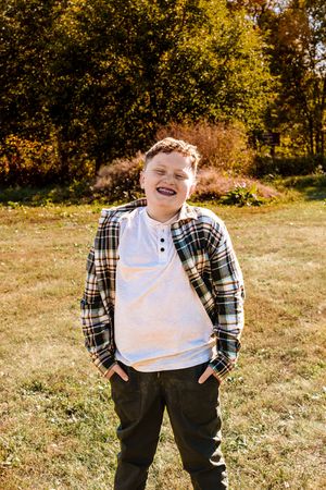 A person wearing a plaid flannel shirt and dark pants stands in a sunny autumn field with golden foliage in background.