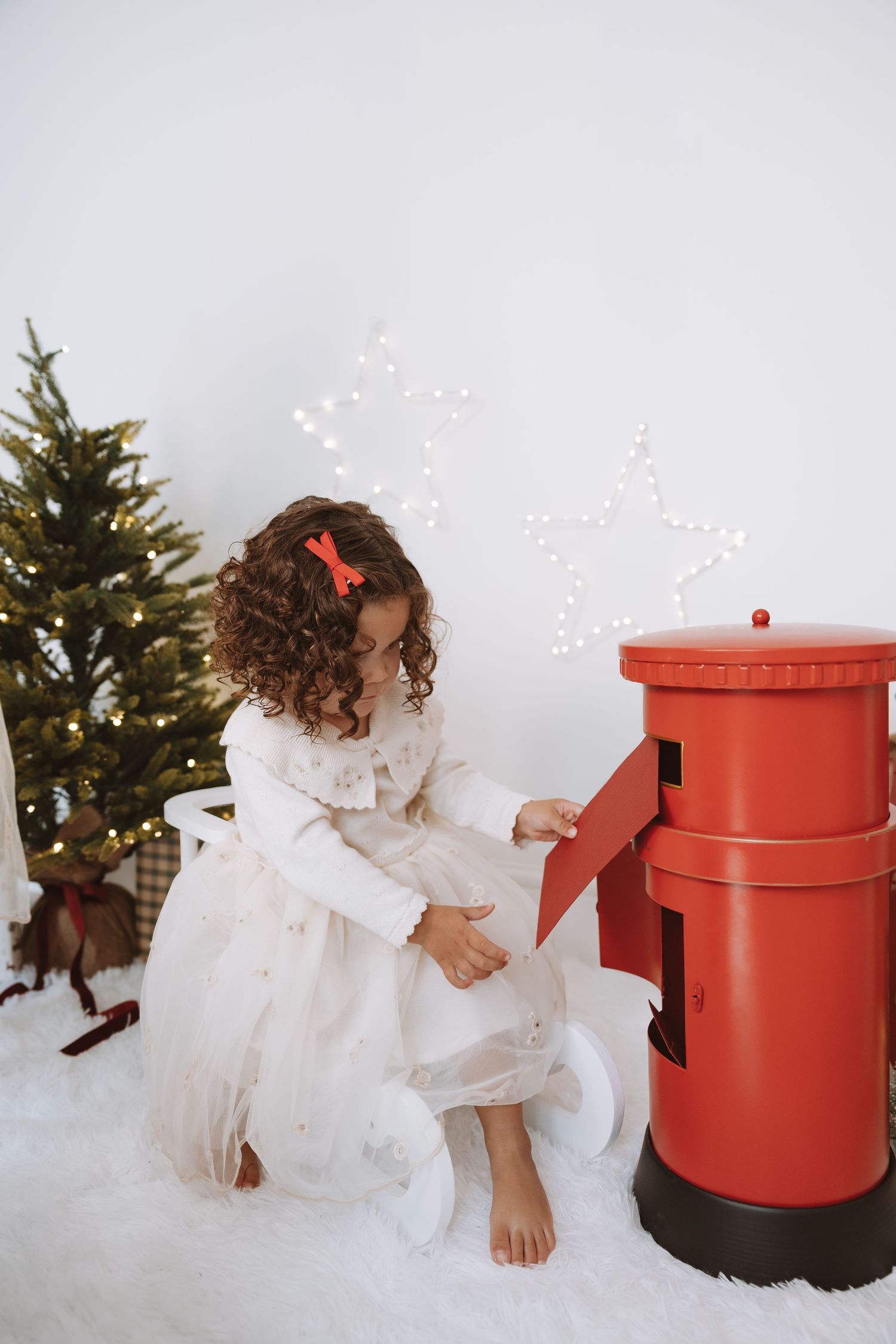 Mother and child in matching white sweaters share joyful moments in a bright minimalist room with holiday decorations.