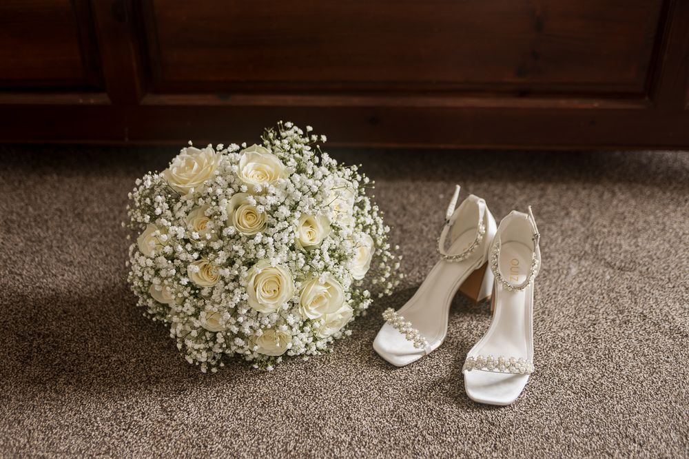 Wedding accessories arranged on carpet with white shoes and floral bouquet.