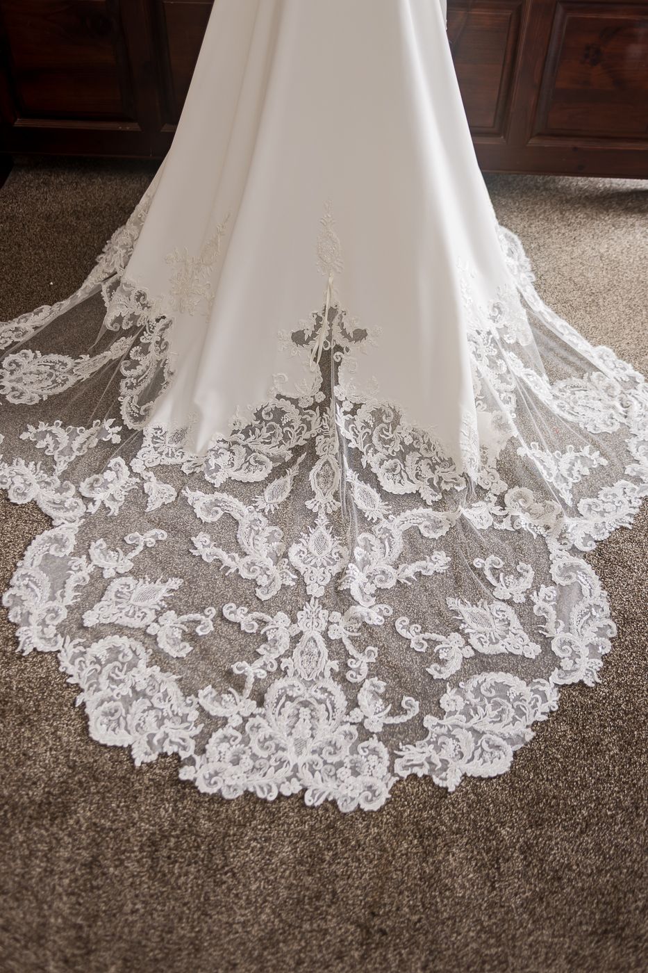 Detailed view of intricate lace pattern on wedding dress train against carpet.