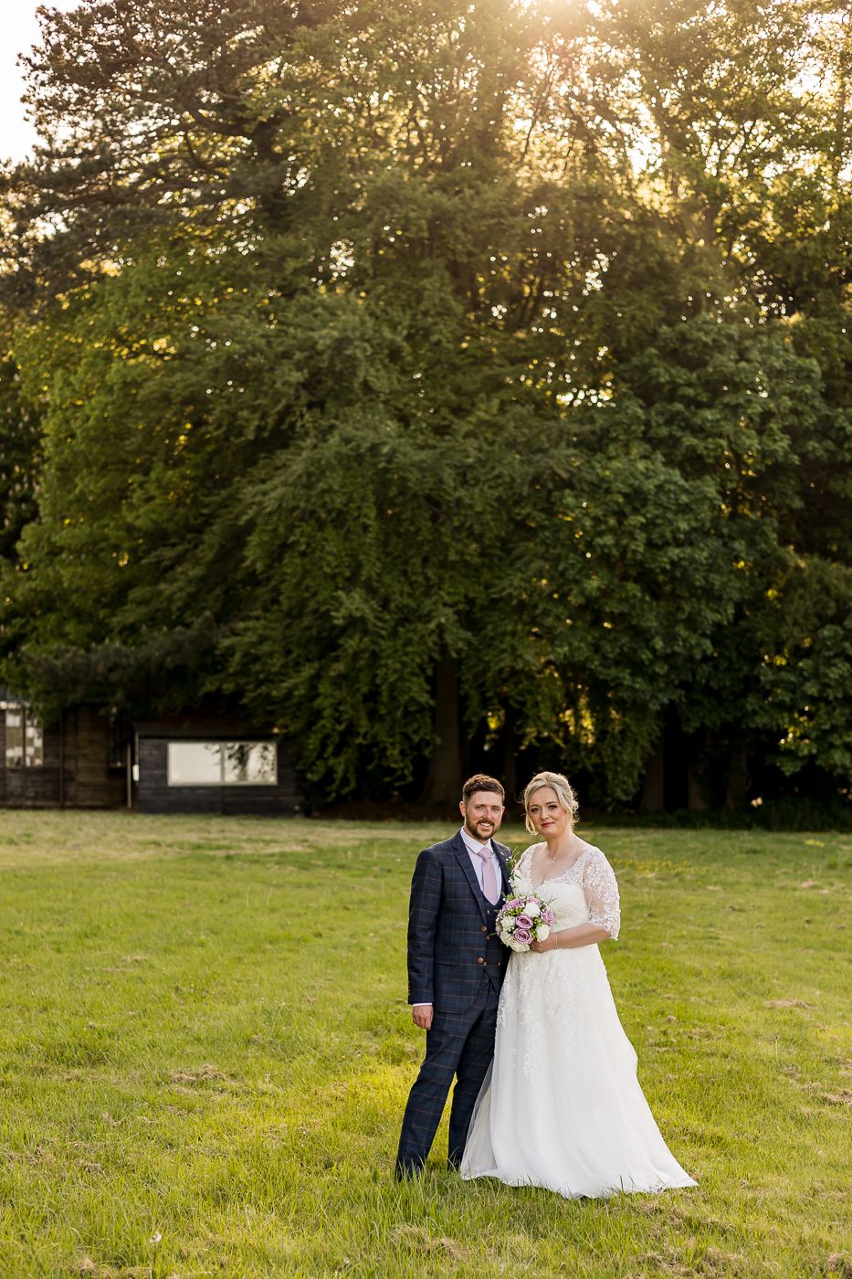 Outdoor wedding portrait in a lush green field during golden hour sunset.